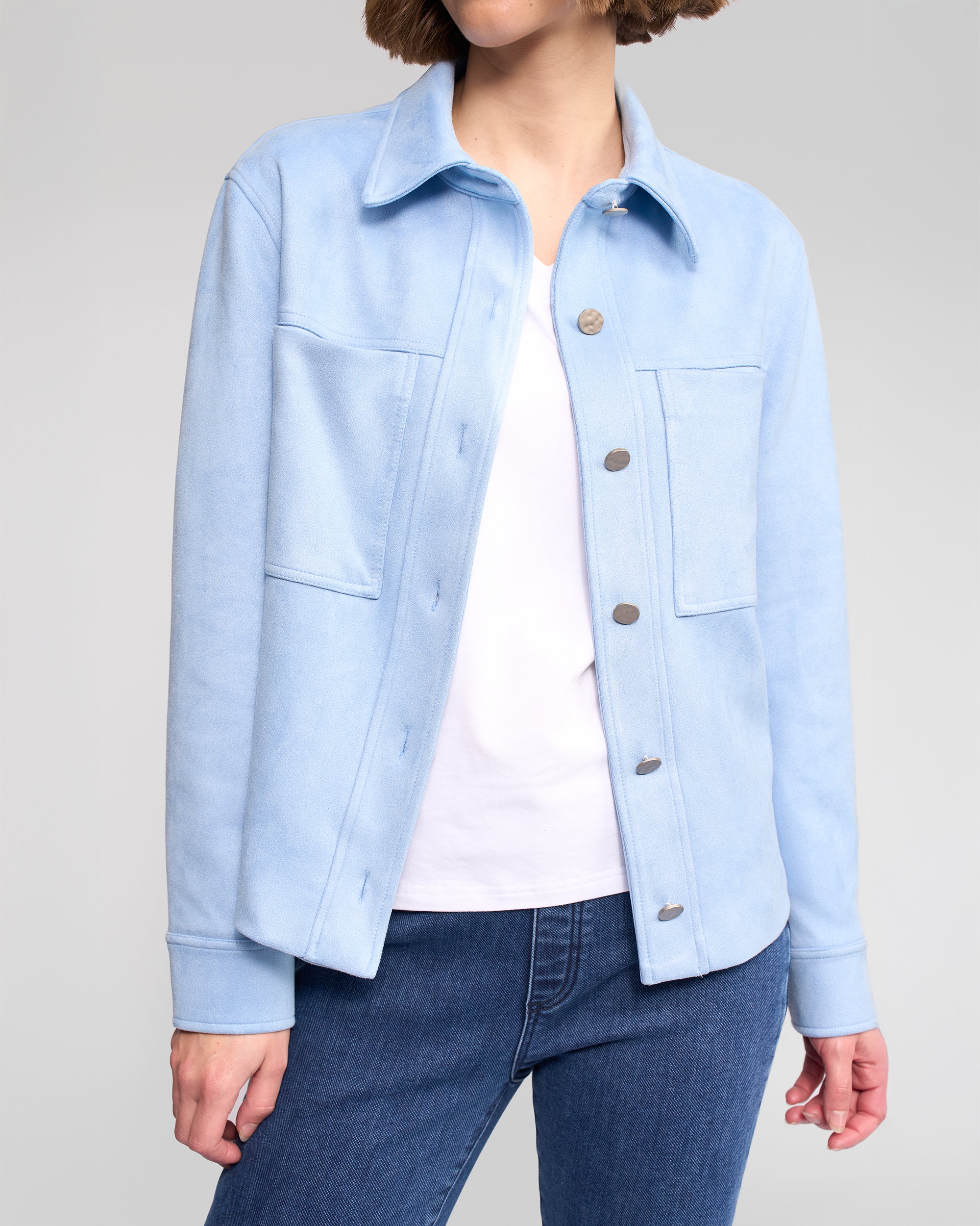 A person models the Vassalli Guest Jacket in Sky Blue over a white t-shirt and blue jeans, standing against a plain light gray background with their face partially out of view.