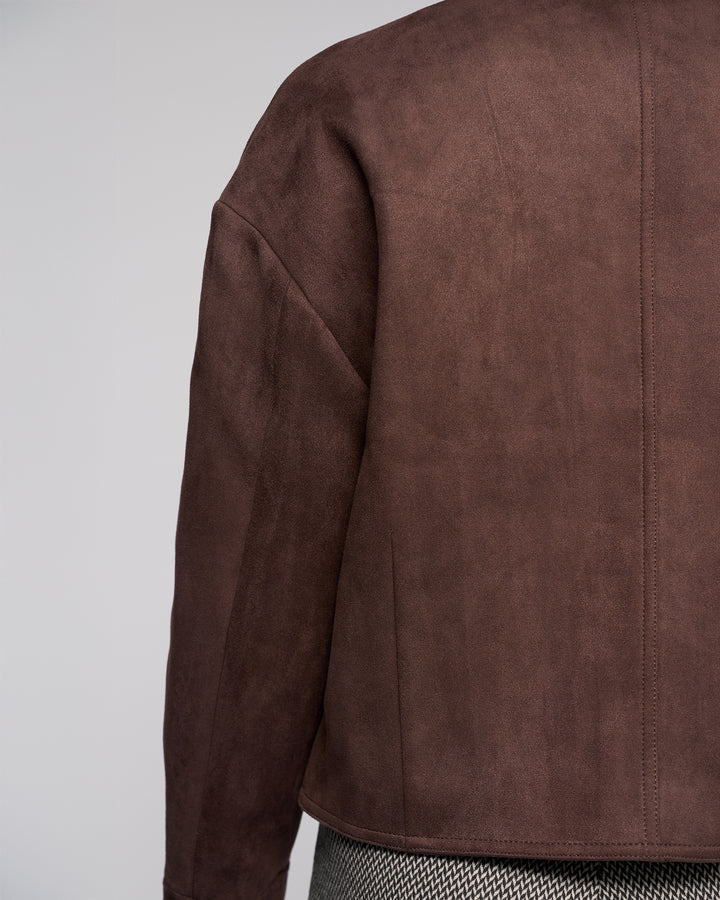 A close-up of the back of a person wearing the Vassalli Relay Jacket in Chocolate and herringbone-patterned pants, set against a plain, light-colored background.