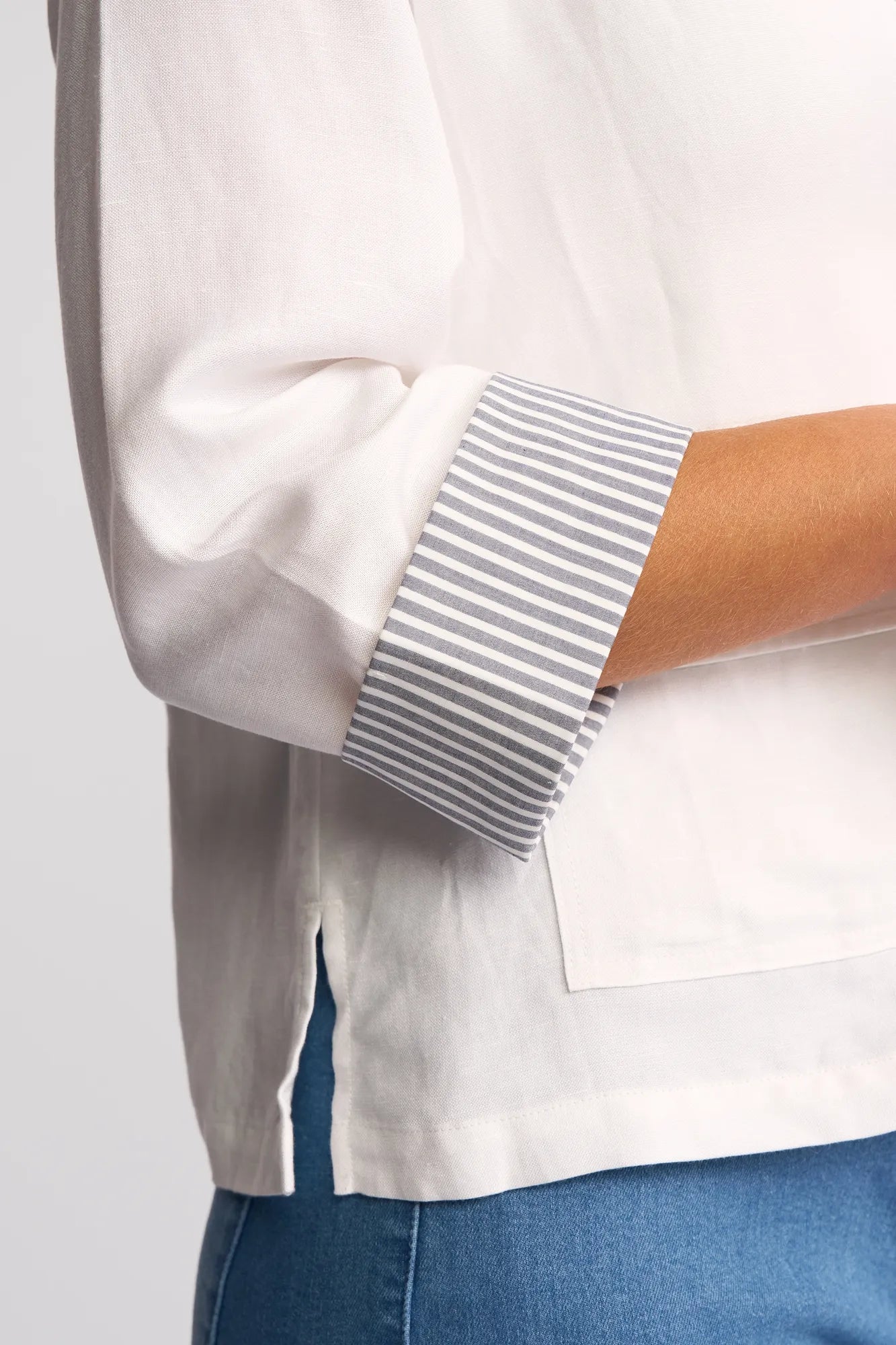 A person wearing the Vassalli Honey Jacket in white, shown from the side, highlighting the blue-and-white striped cuffs and detailed sleeve—crafted from a lightweight linen-viscose blend for a comfortable yet polished look.