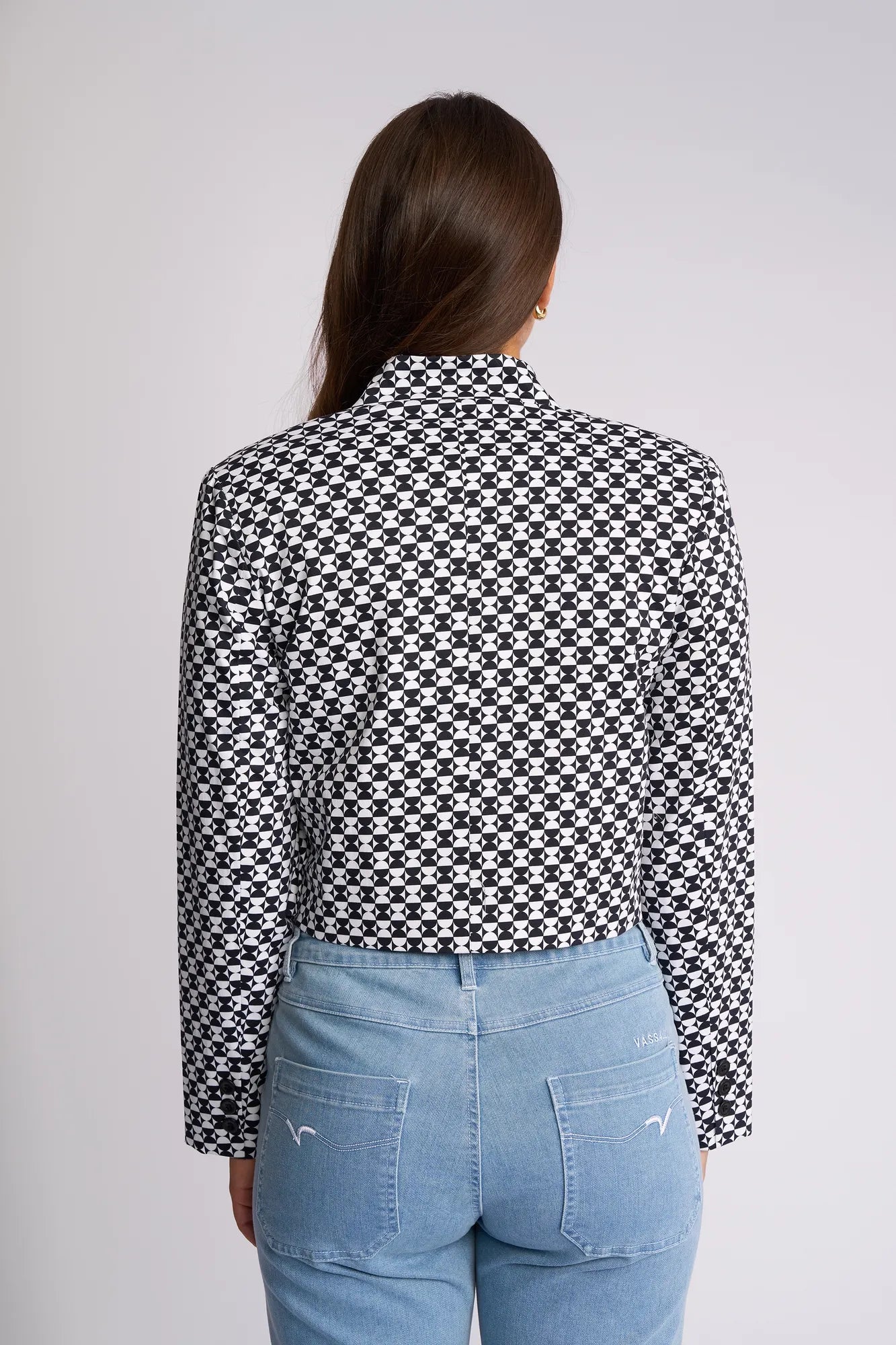 A person with long brown hair, seen from behind, wears the Vassalli Midas Jacket - Dixie and light blue jeans against a plain light background.