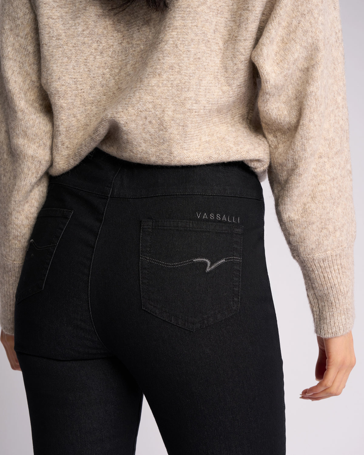 A person wearing a beige sweater and Vassalli Origin Pull On - Black Denim jeans, shown from the back highlighting the pocket detailing and Vassalli branding.