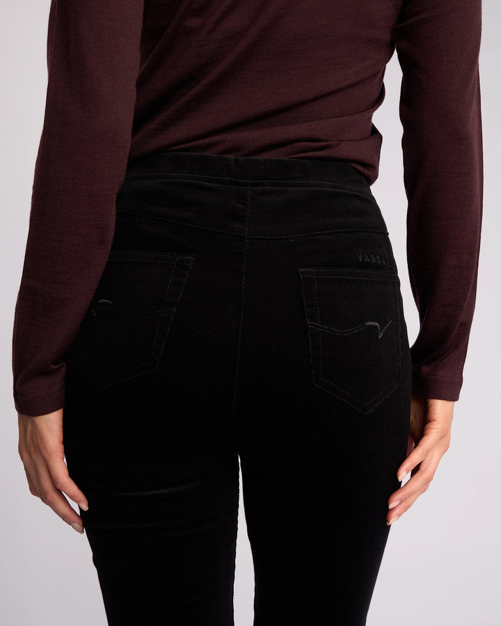 A person is shown from the back wearing a long-sleeve, dark burgundy top paired with Vassalli Origin Cord Pull On skinny-leg pants in black, featuring a high waist and two back pockets, hands resting by their sides.