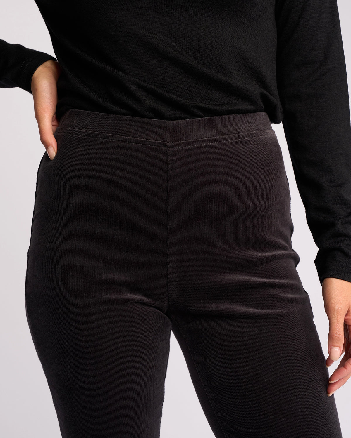 A person models the Vassalli Origin Cord Pull On - Charcoal, shown from shoulders to mid-thigh, with one hand on their hip and the other by their side.