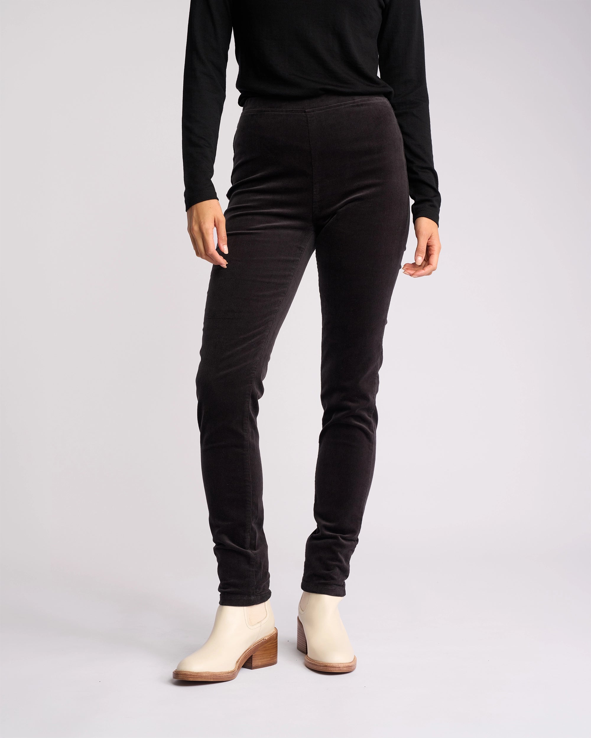 A person stands against a plain white background wearing a black long-sleeve top and Vassalli’s Origin Cord Pull On - Charcoal. Their head is not visible in the image.