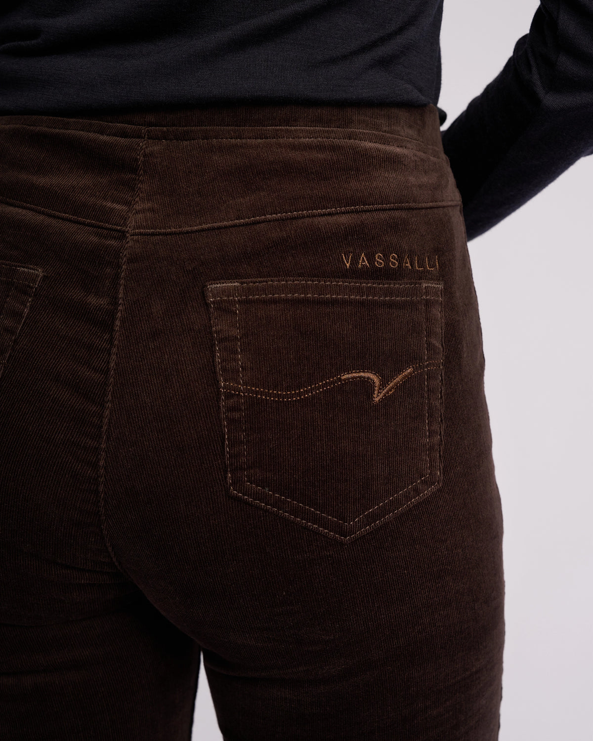 Close-up of a person wearing Vassalli Origin Cord Pull On pants in Walnut with the Vassalli logo above the back pocket, paired with a black top.