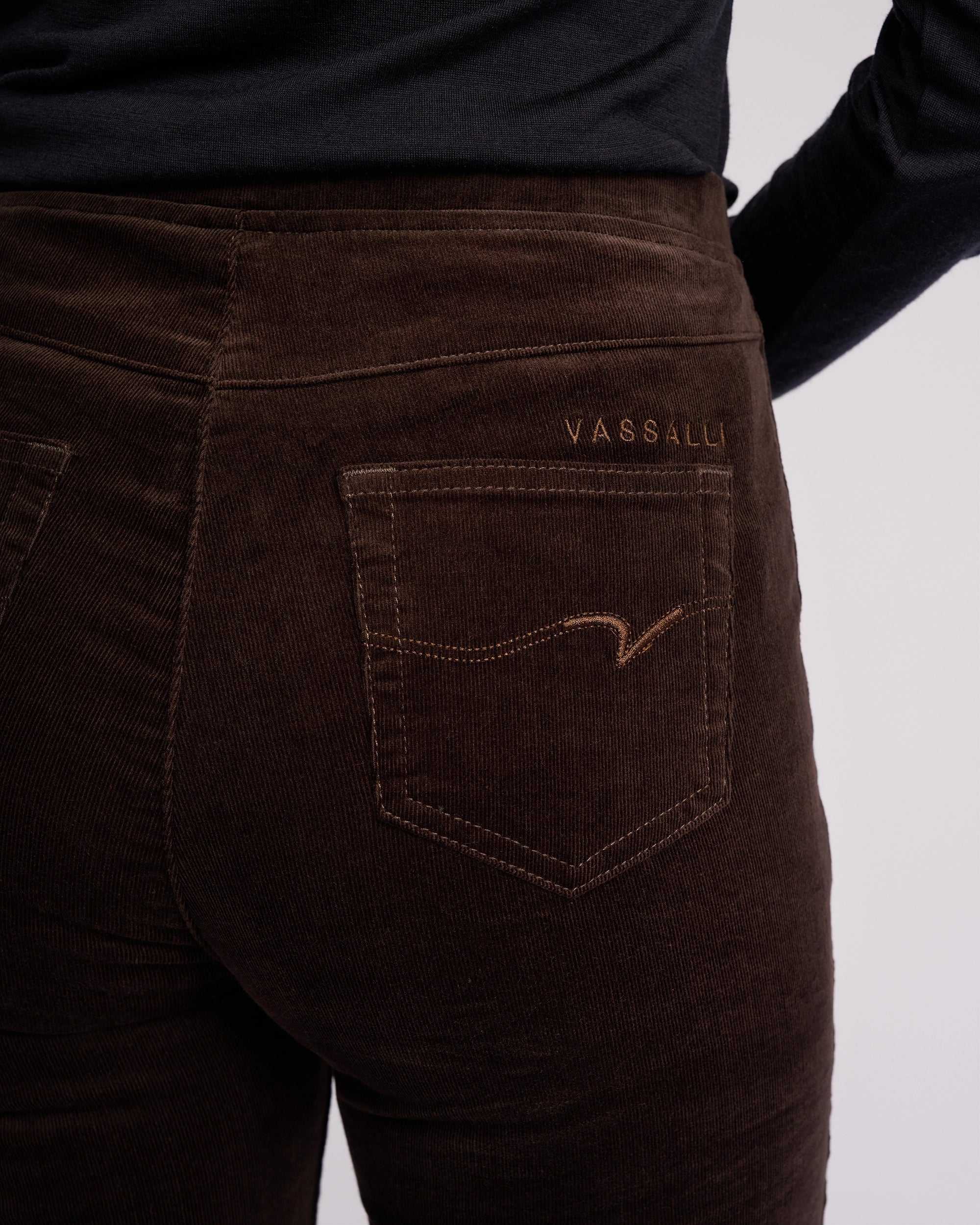 Close-up of a person wearing Vassalli Origin Cord Pull On pants in Walnut with the Vassalli logo above the back pocket, paired with a black top.
