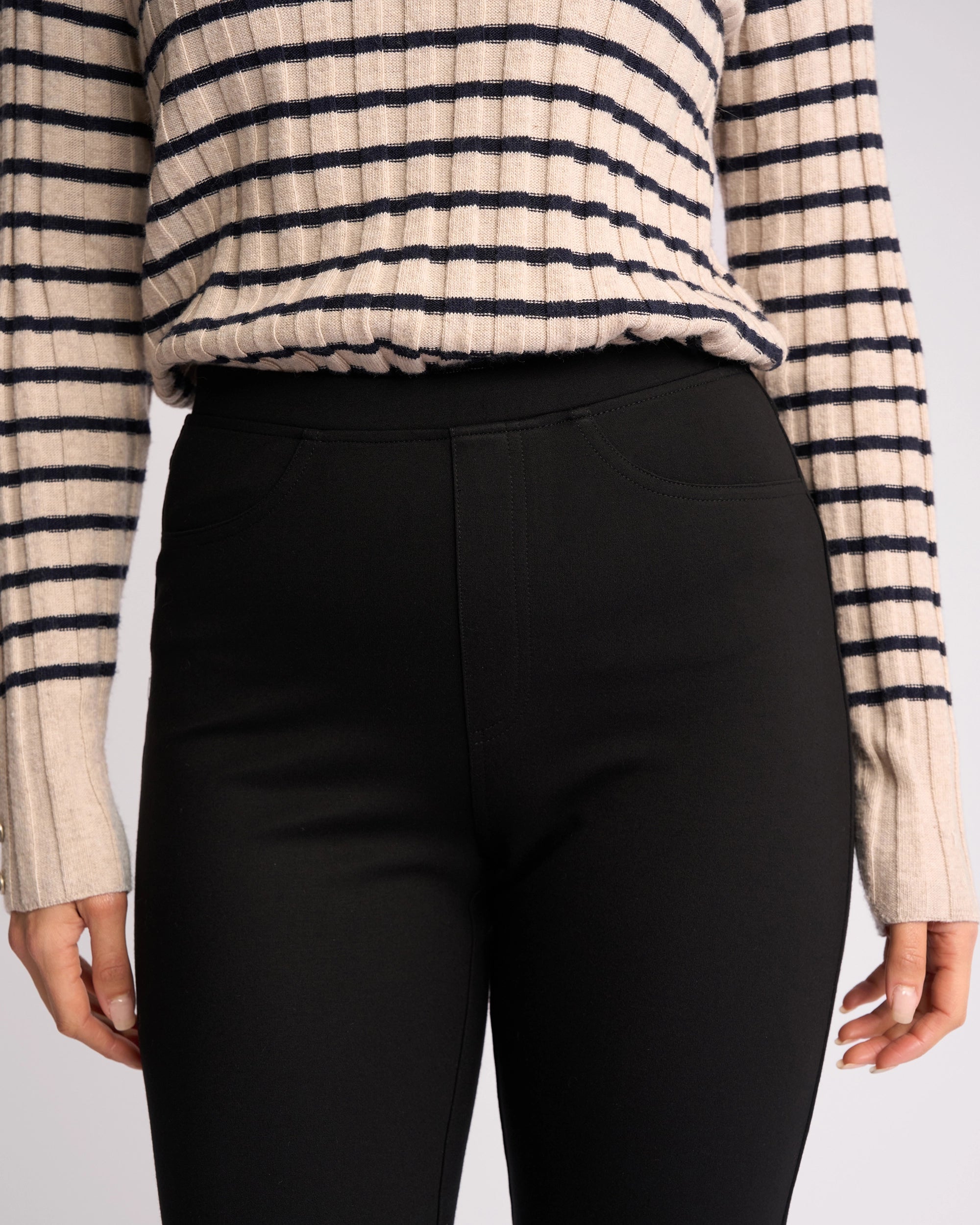 A person wears a beige and black striped long-sleeve top tucked into Vassalli Bay Ponti Pull On - Black slim-leg workwear pants, with only the torso and upper legs visible.