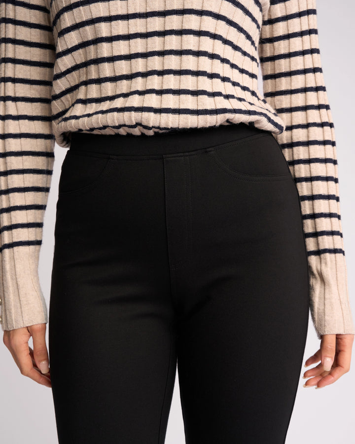 A person wears a beige and black striped long-sleeve top tucked into Vassalli Bay Ponti Pull On - Black slim-leg workwear pants, with only the torso and upper legs visible.