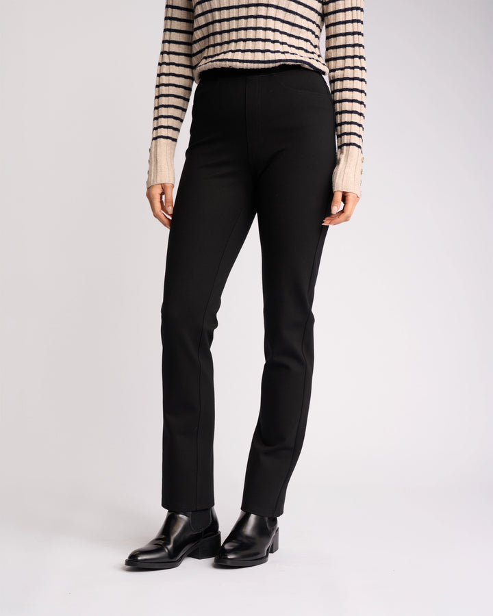 A person wearing Vassalli’s Bay Ponti Pull On - Black pants stands against a plain light background, paired with a beige and black striped sweater and black ankle boots. The image is cropped at the shoulders.
