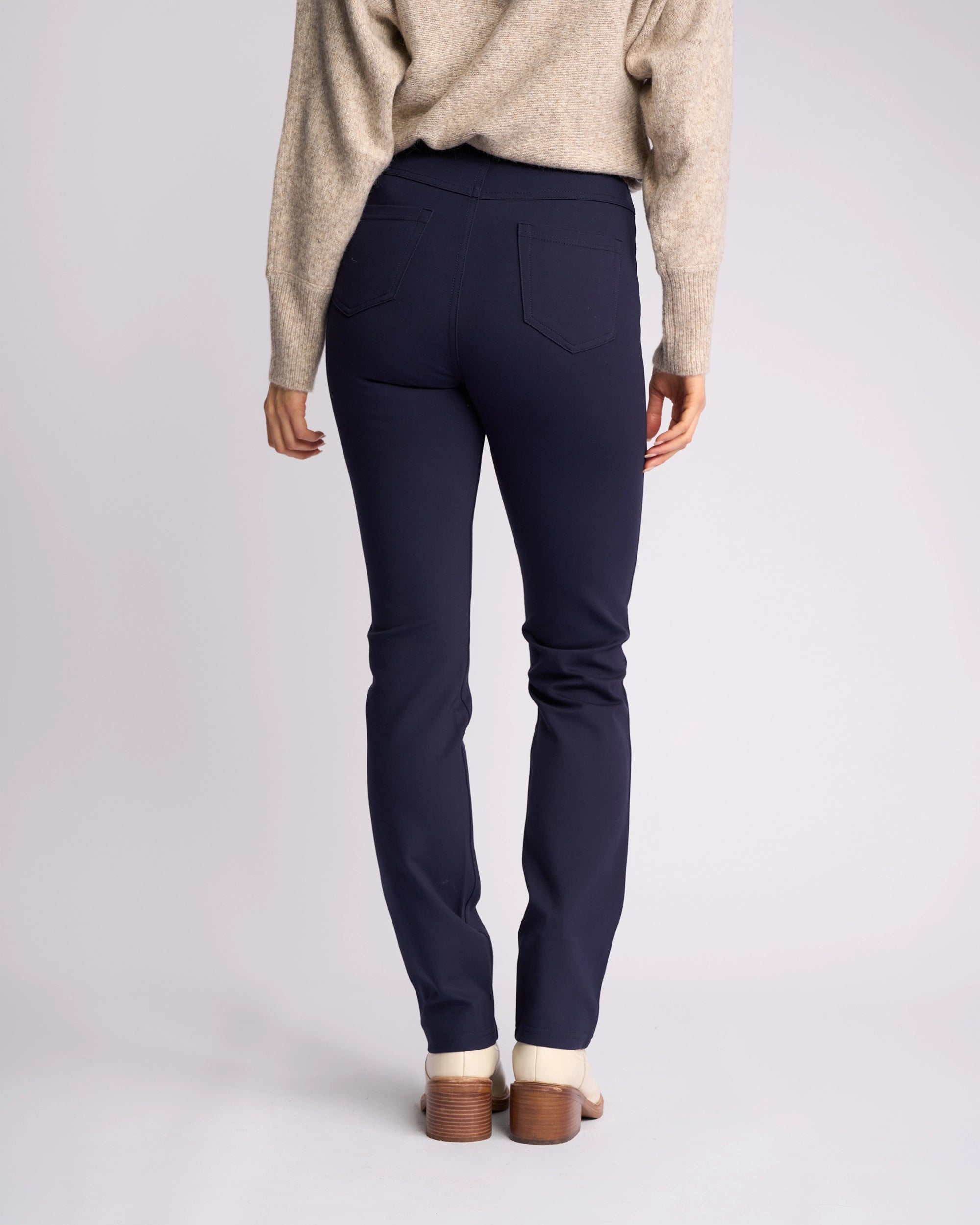 A person is seen from behind wearing Vassalli's Bay Ponti Pull On pants in navy with a beige sweater and cream heeled shoes, standing against a plain light background for an effortless workwear look.