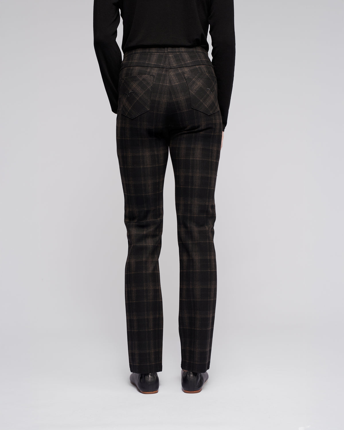 A person is seen from behind in Vassalli's Bay Pull On - Checkmate pants, a black long-sleeve top, and black shoes, standing against a plain light gray background.