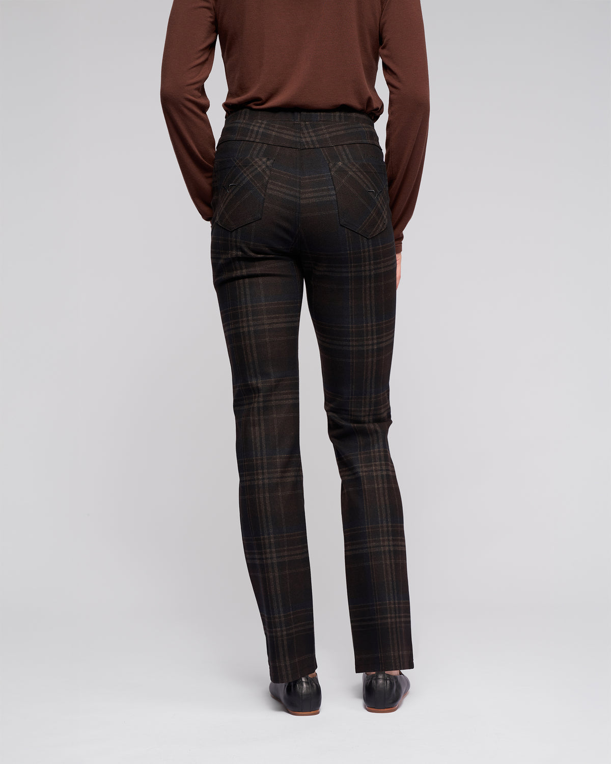 A person stands facing away from the camera in a brown long-sleeve top and Vassalli Bay Pull On - Hugo dark plaid slim pants with back pockets, straight-leg fit, and elasticated waistband. The background is plain light grey.
