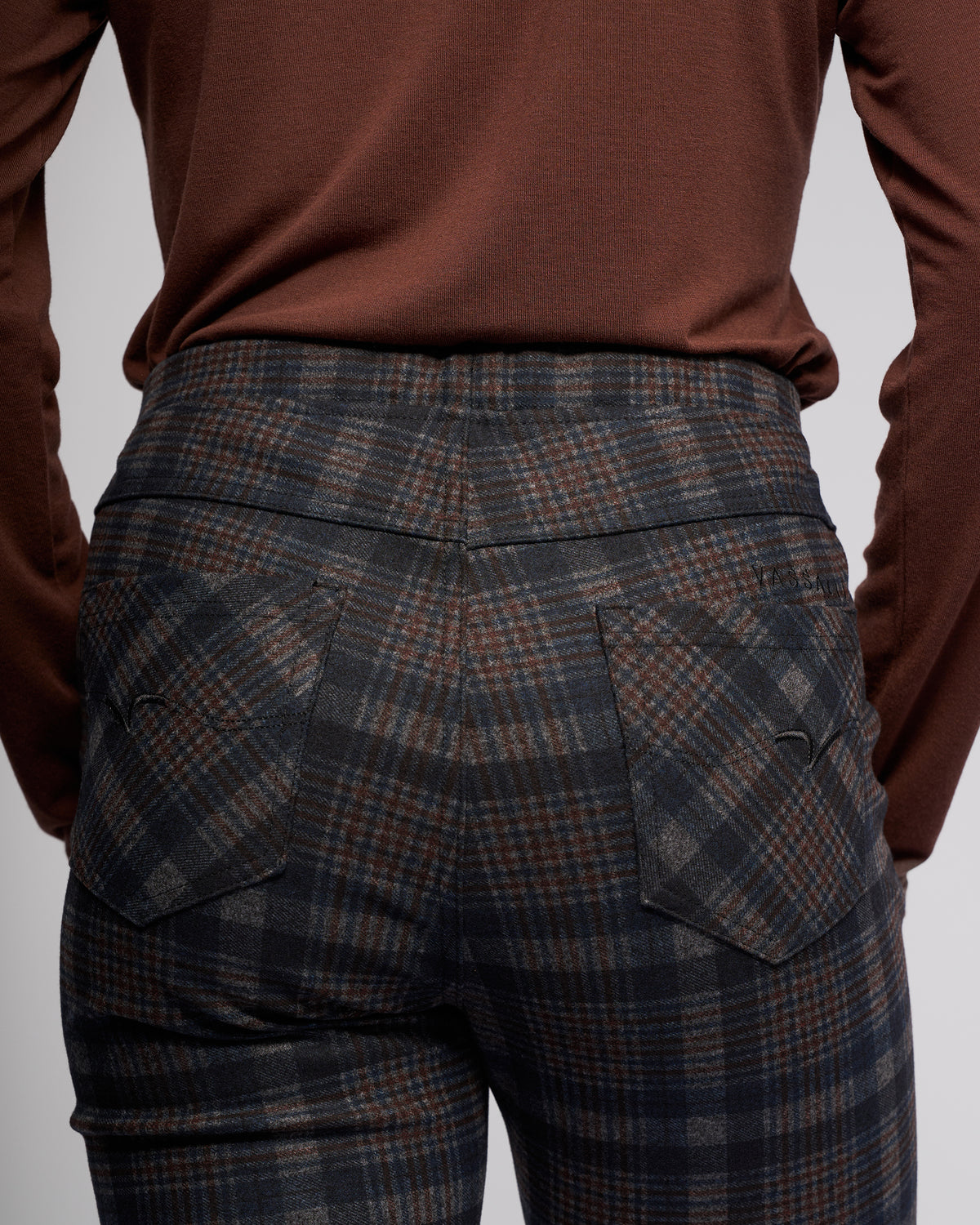 Model showcases the Vassalli Bay Pull On - Nomad, a high-waisted slim pant in dark plaid, paired with a brown long-sleeve top. Rear view emphasizes the pattern and stretch ponti fabric for comfort.