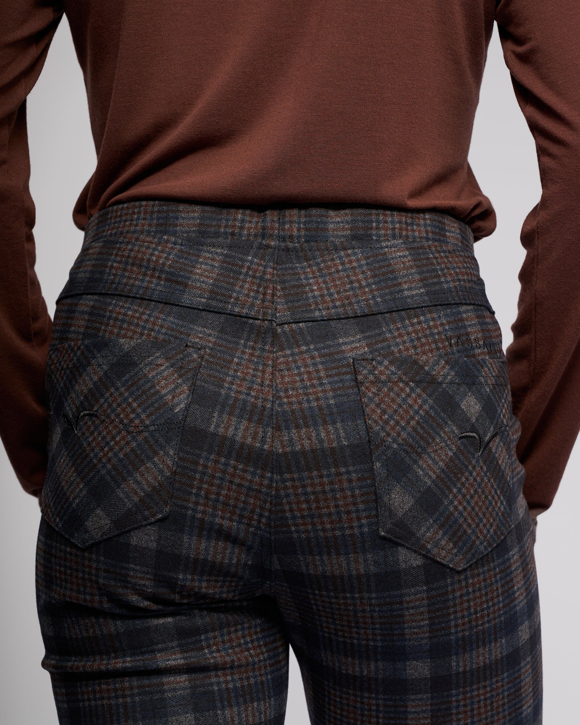Model showcases the Vassalli Bay Pull On - Nomad, a high-waisted slim pant in dark plaid, paired with a brown long-sleeve top. Rear view emphasizes the pattern and stretch ponti fabric for comfort.