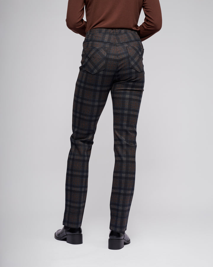 A person wears the Vassalli Bay Pull On - Nomad pants with a long-sleeve brown top and black shoes, facing away to showcase the back of the pants against a plain, light-colored background.
