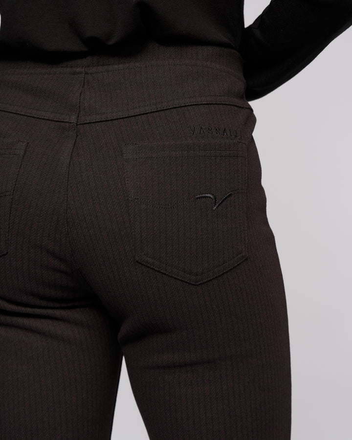 Close-up of a person wearing Vassalli Bay Pull On - Metro dark, pinstriped slim pants and a black top, featuring the back pocket with the brand name stitched above it.