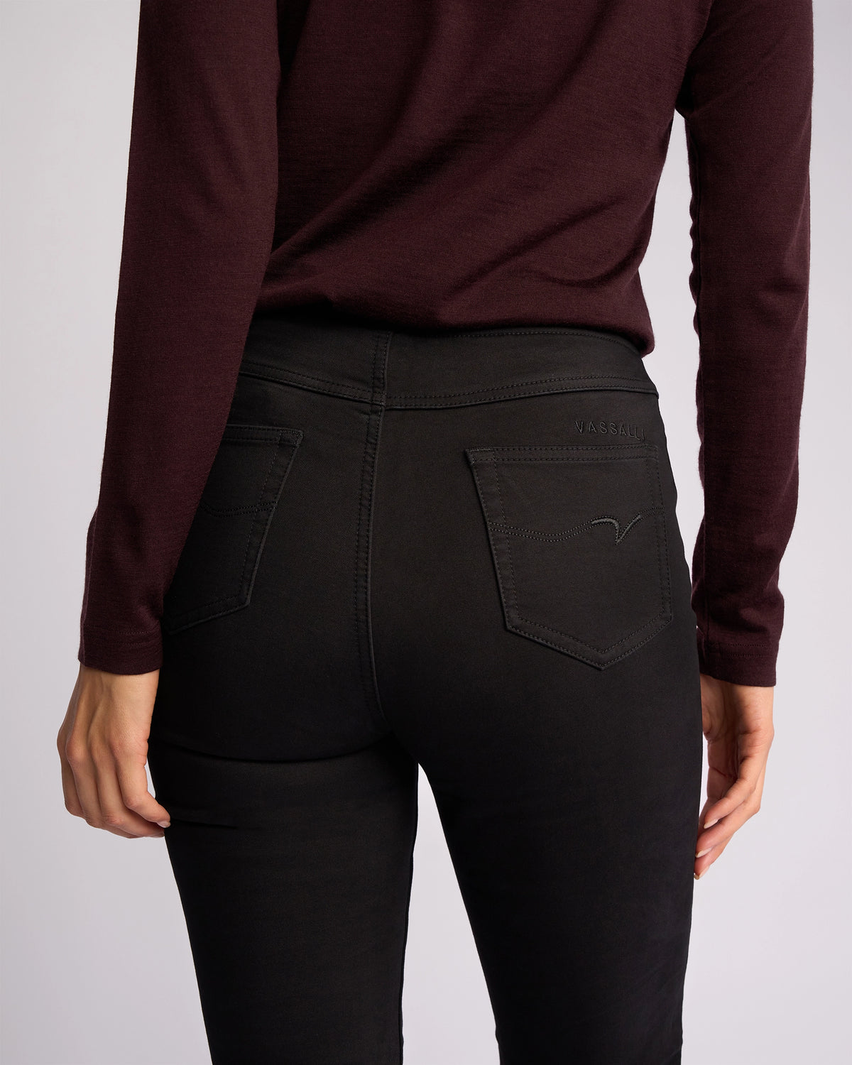 A person is shown from the back wearing Vassalli’s Bay Knit Pull On - Black pants, with one hand at their side. The focus highlights the pocket details of these slim-leg, stretch fabric pants.