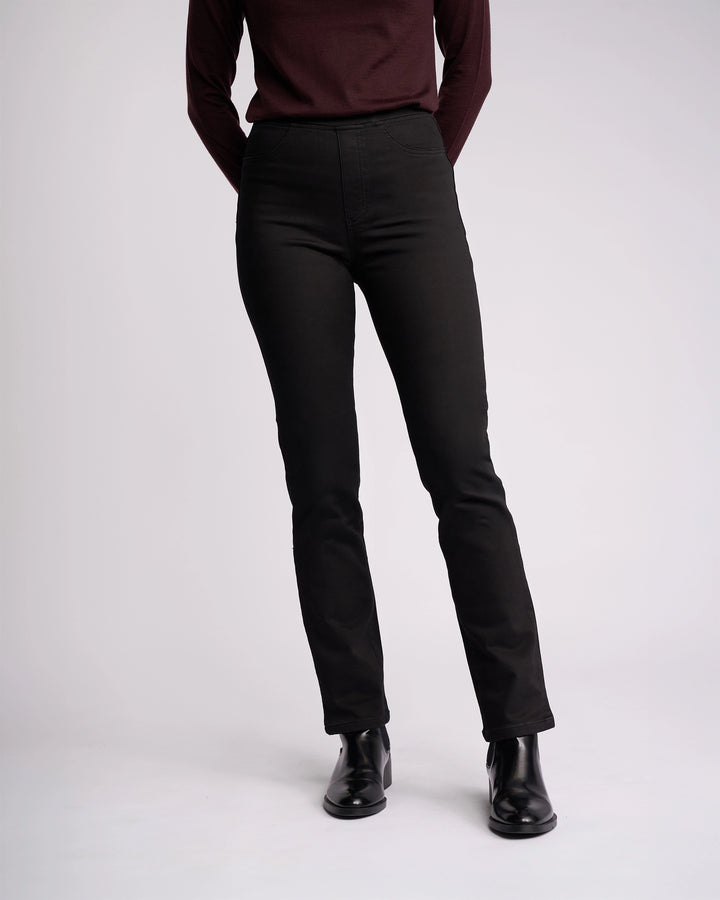 A person wears the Vassalli Bay Knit Pull On - Black pants with a long-sleeve burgundy top and black ankle boots, standing against a light background. The upper part of their face is not visible.