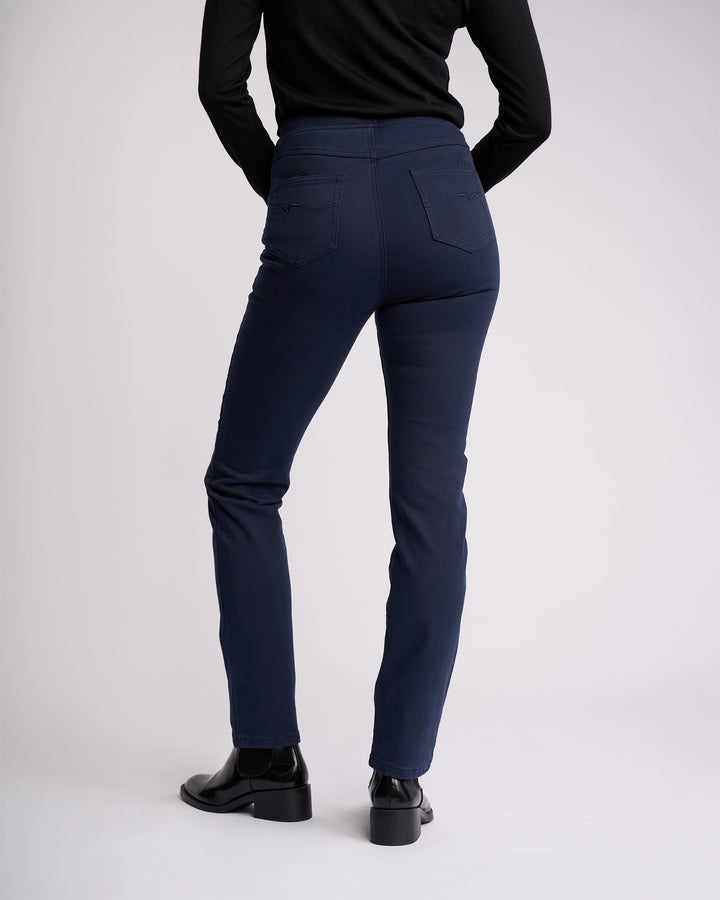 A person in the Vassalli Bay Knit Pull On - Carbon stands with their back to the camera, wearing a black long-sleeve top and black ankle boots against a plain light background.