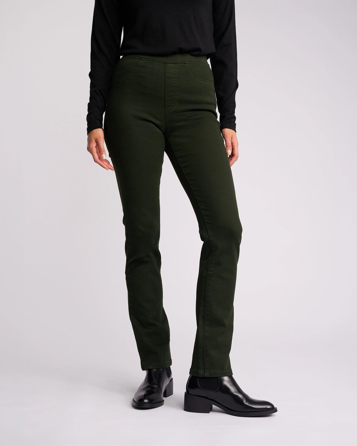 A person wearing a black long-sleeve top, Vassalli Bay Knit Pull On - Forest pants, and black ankle boots stands against a plain light background, with their head not visible in the image.