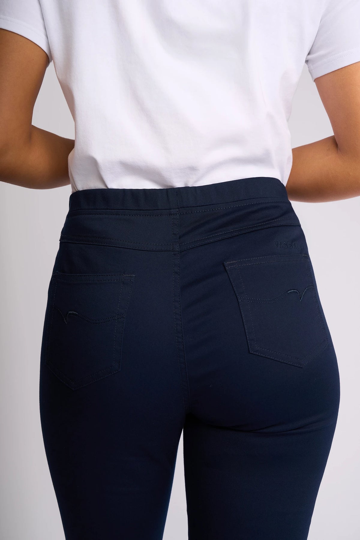 A person wearing a white T-shirt and Vassalli Bay Pull On - Navy slim leg pants, shown from the back with a focus on the pockets and waistband of the stretch fabric jeans.