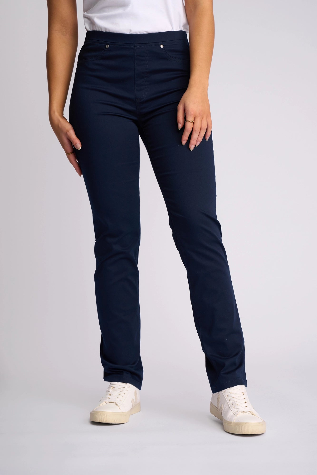 Model wears Vassalli’s Bay Pull On - Navy, a full-length, straight-leg pant crafted from stretch fabric, styled with white sneakers and a white short-sleeve shirt against a plain light grey background.