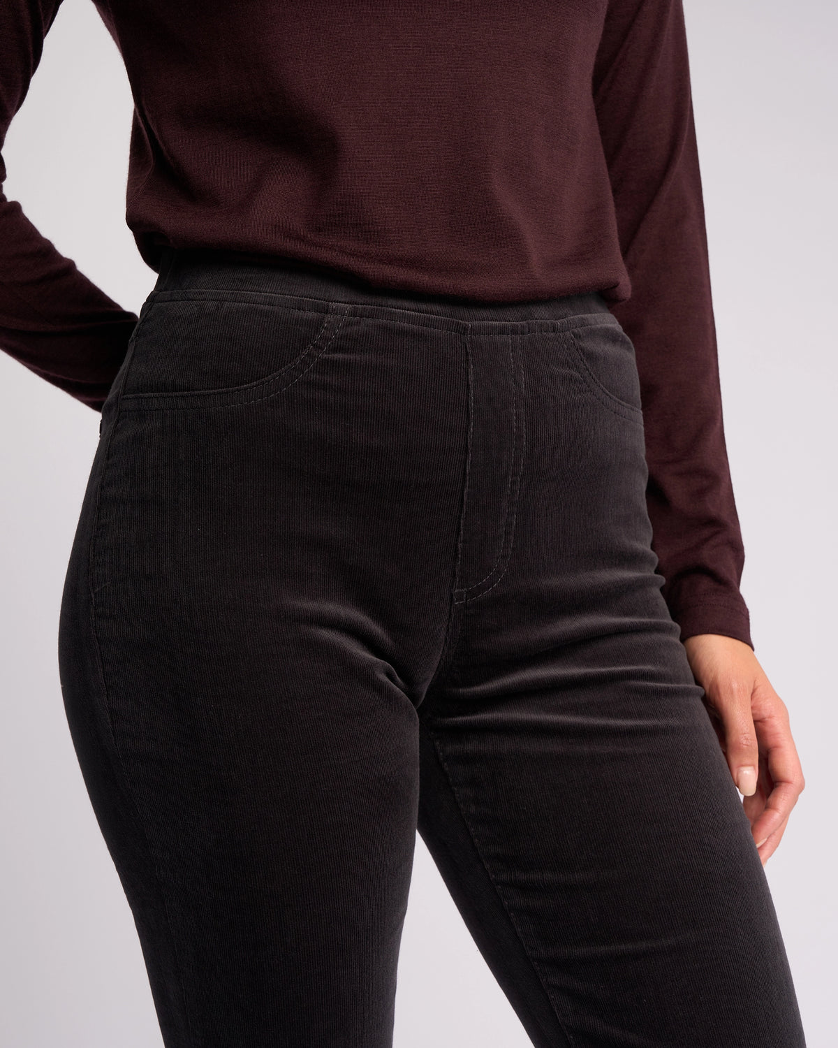 A person models the Vassalli Bay Cord Pull On - Charcoal pants, shown from chest to mid-thigh with one hand by their side against a plain background.