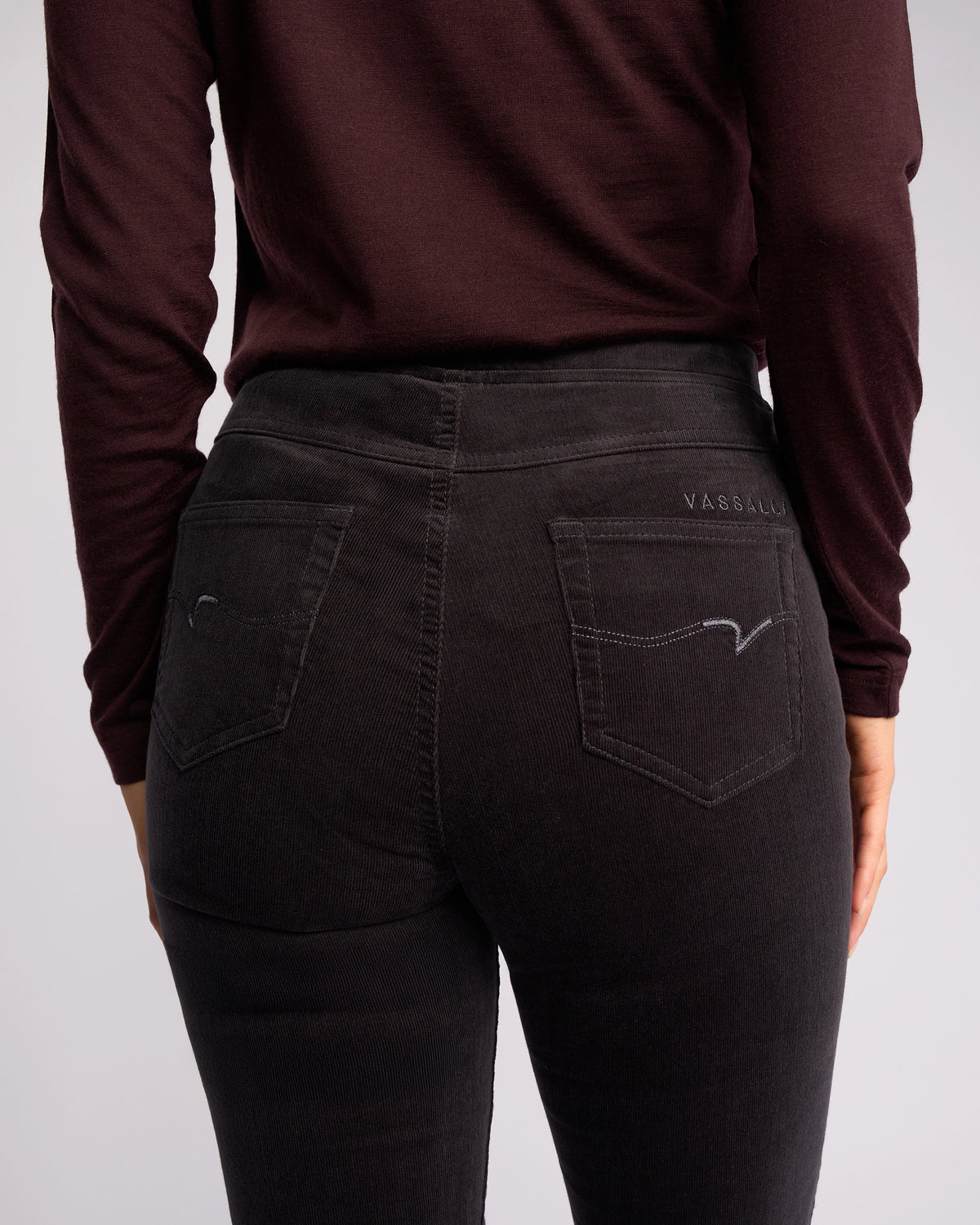 A person is shown from the back wearing the Vassalli Bay Cord Pull On - Charcoal, focusing on the rear pockets and stitched detailing of these slim-leg cord pants.