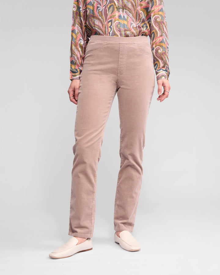 A person wears Vassalli Bay Cord Pull On - Twig pants, a colorful wavy long-sleeve shirt, and cream slip-on shoes, standing against a plain light background. Only the lower half of the body is visible.