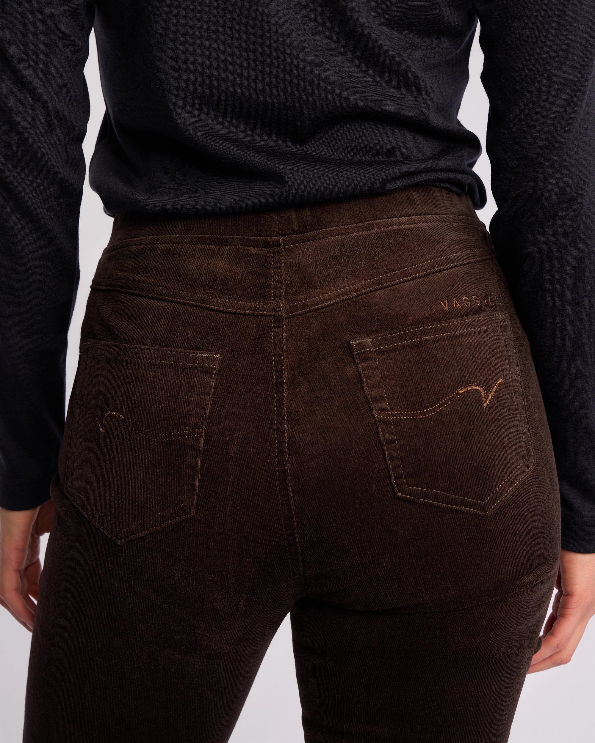 A person wearing Vassalli Bay Cord Pull On pants in Walnut and a black long-sleeve shirt, shown from the back with focus on the pant's waistband and pockets.