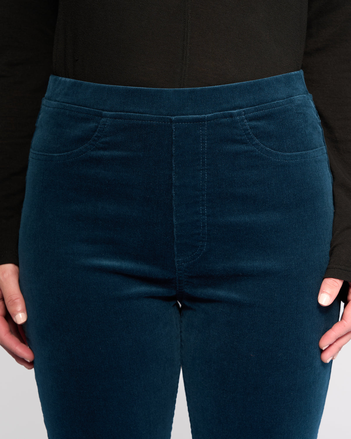 A person wears Vassalli's Bay Cord Pull On pants in Petrol and a long-sleeved black top, shown waist to mid-thigh, with hands relaxed at their sides.