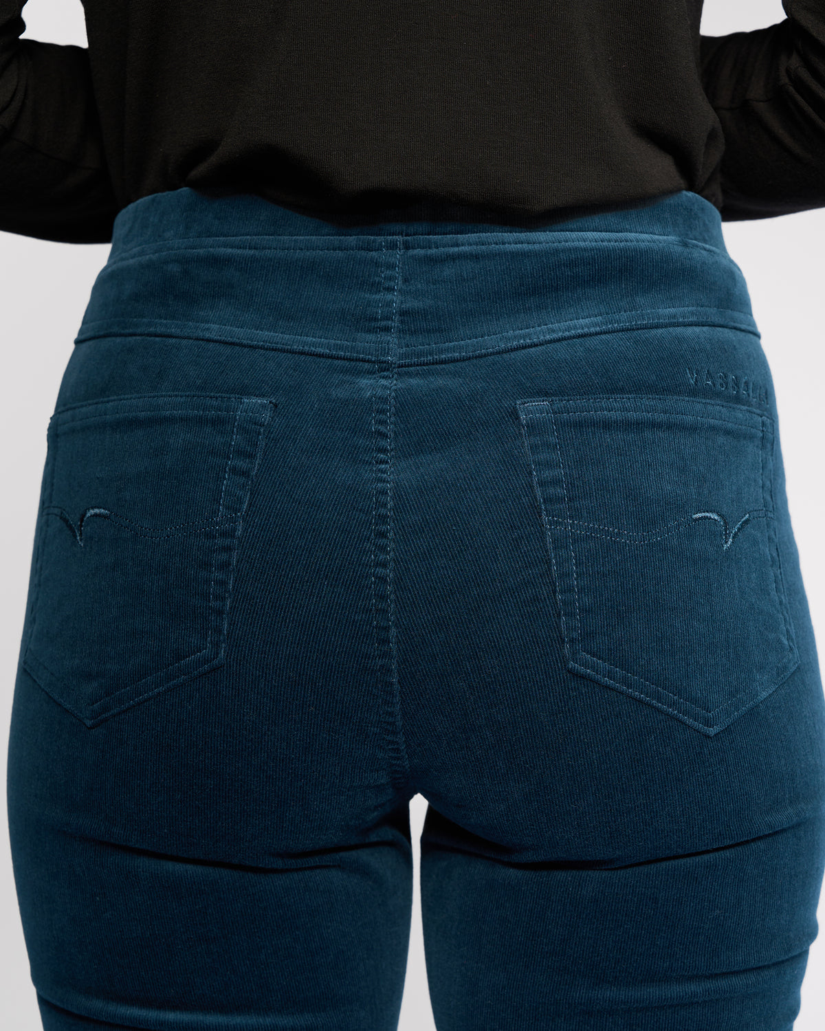 A person is shown from the back wearing Vassalli's Bay Cord Pull On pants in Petrol, styled with a black top to showcase the high waist, slim fit, pocket detail, and subtle stretch texture.