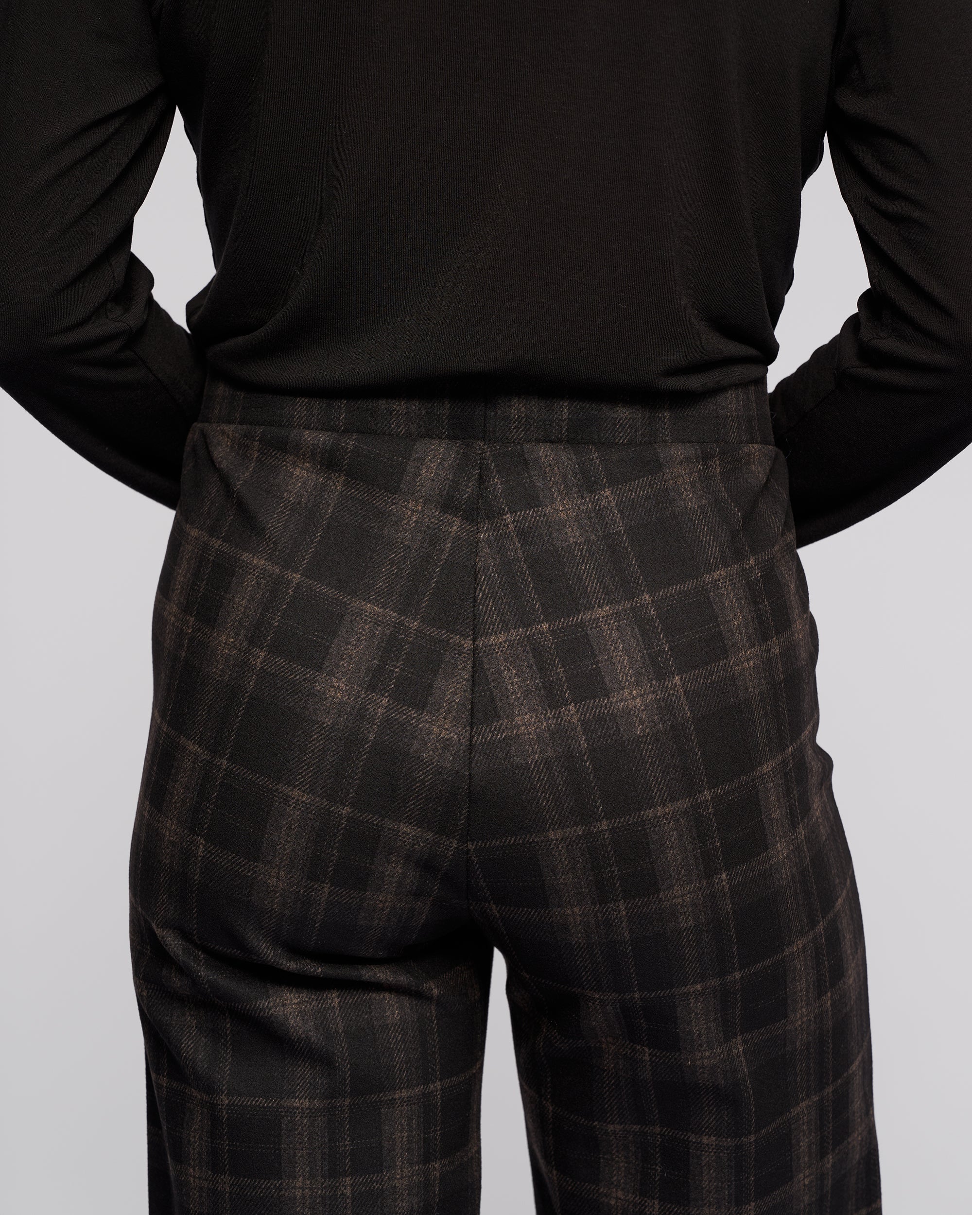A person is shown from the back wearing Vassalli's Loft Pull On - Checkmate wide-leg pants and a black long-sleeve top, with focus on the lower back and upper legs against a plain light background.