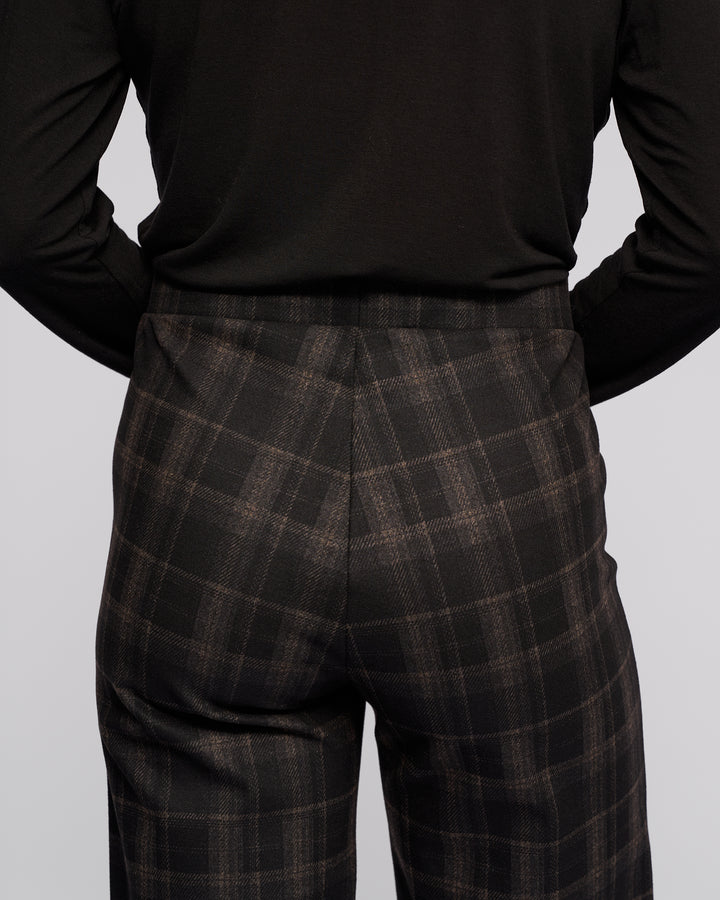 A person is shown from the back wearing Vassalli's Loft Pull On - Checkmate wide-leg pants and a black long-sleeve top, with focus on the lower back and upper legs against a plain light background.