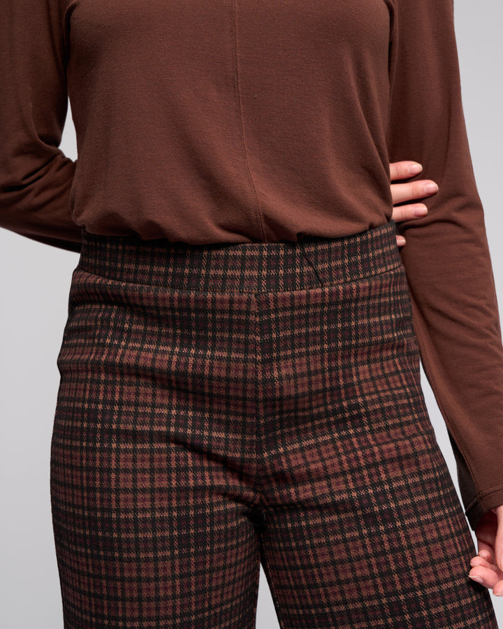 Someone stands against a neutral background with one hand on their hip, wearing the Vassalli Loft Pull On - Cherry pants featuring a high waist, wide-leg fit, plaid pattern, and elasticated waistband.