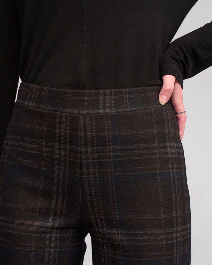 Wearing Vassalli's Loft Pull On - Hugo pants, a person stands with one hand on their hip in high-waisted, dark plaid wide-leg trousers and a black long-sleeve top, showcasing a silver ring.