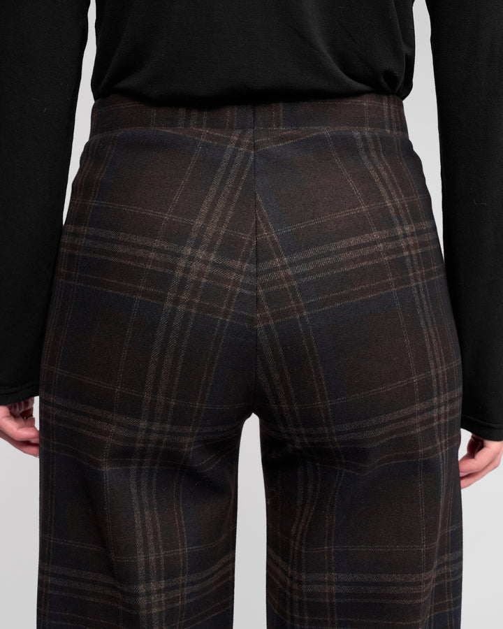 A person wearing Vassalli Loft Pull On - Hugo dark brown and black plaid wide-leg pants in a comfortable pull-on style with a black long-sleeve shirt, shown from the back waist down to upper thighs.