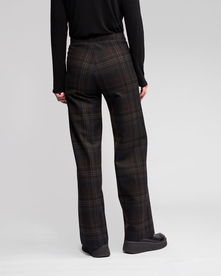 A person faces away, wearing Vassalli's Loft Pull On - Hugo dark plaid wide-leg pants with a black long-sleeve top and black platform shoes, set against a plain light background.