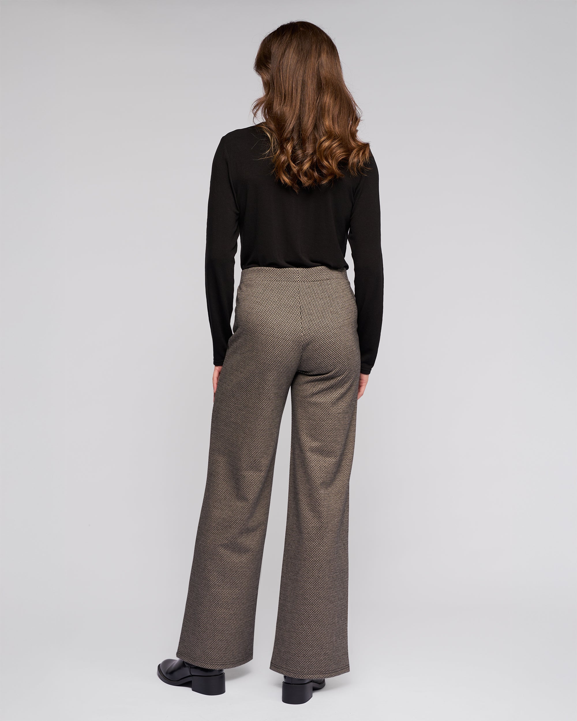 A person with wavy brown hair models the Vassalli Loft Pull On - Knox black long-sleeve top and stretch knit wide-leg pant, standing with their back to the camera against a plain light background.