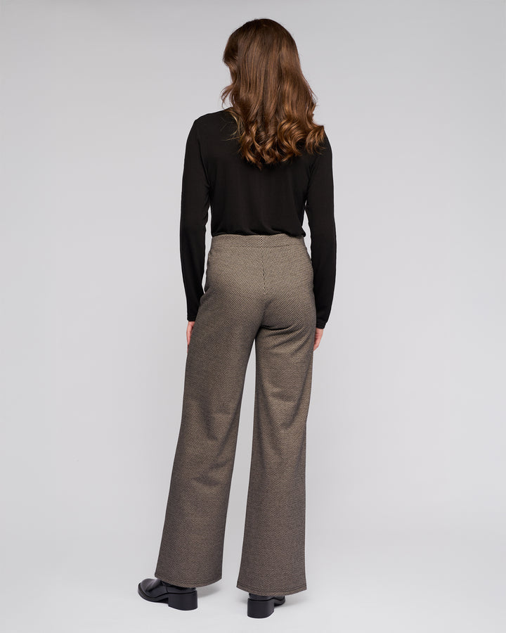 A person with wavy brown hair models the Vassalli Loft Pull On - Knox black long-sleeve top and stretch knit wide-leg pant, standing with their back to the camera against a plain light background.