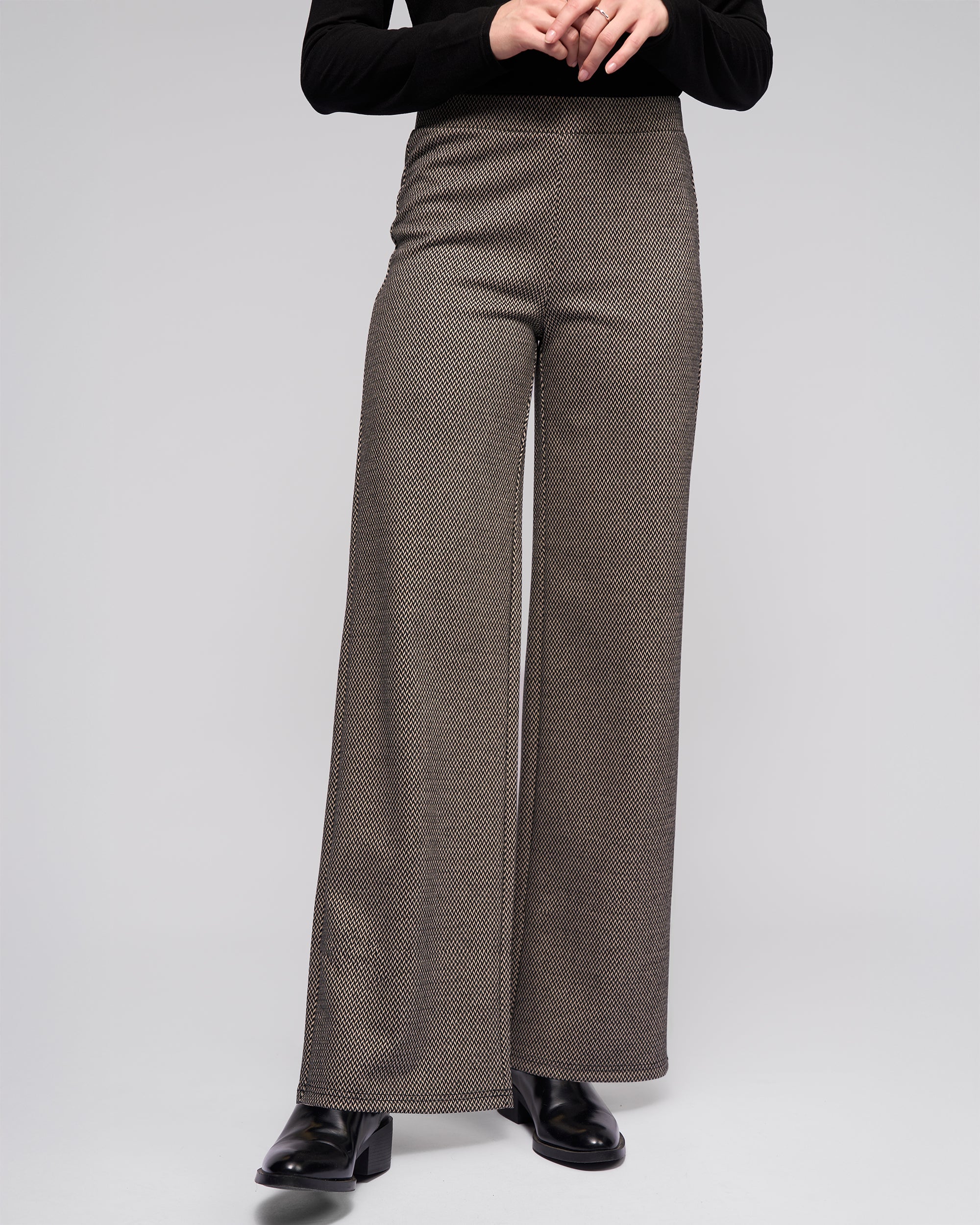 Wearing Vassalli's Loft Pull On - Knox high-waisted, wide-leg black/oat check pants and a black long-sleeve stretch knit top, a person stands with hands clasped at the waist against a plain light background.