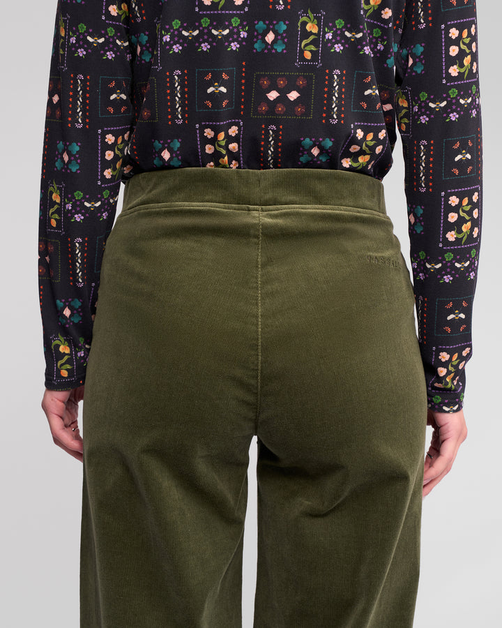 A person shown from the back, waist to mid-thigh, is wearing Vassalli's Loft Cord Pull On pants in Deep Sage and a long-sleeve black shirt with a colorful floral and geometric pattern.