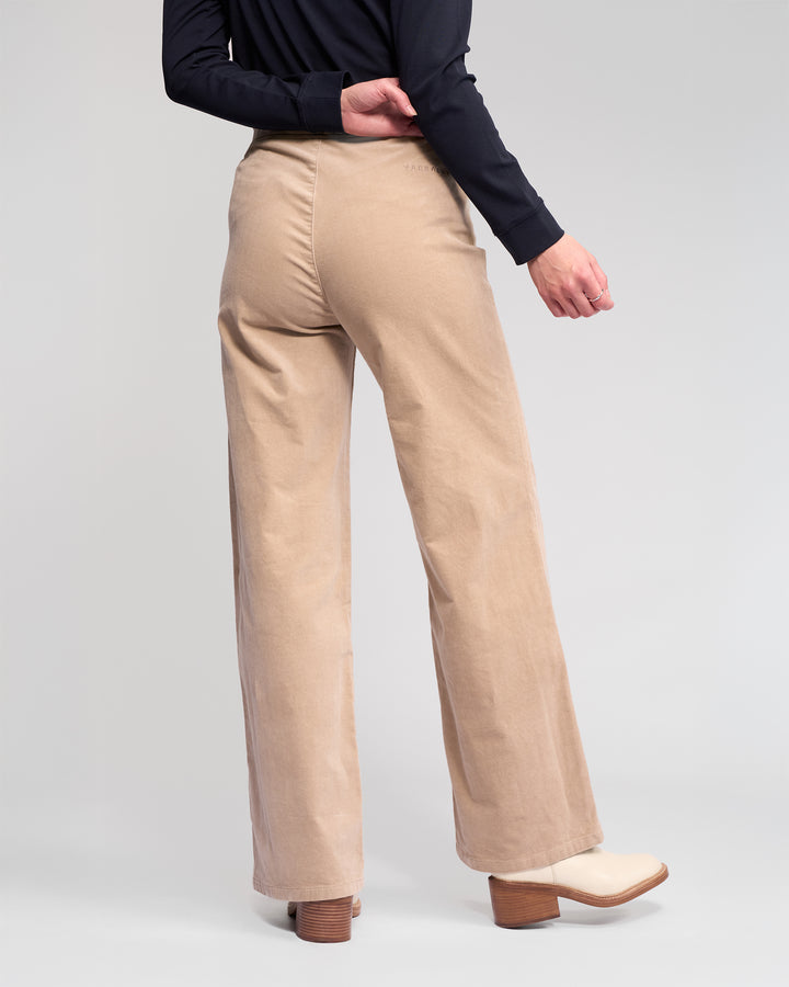 A person shown from the back wears Vassalli’s Loft Cord Pull On - Oat pants, a black long-sleeve top, and light heeled boots against a plain light background.