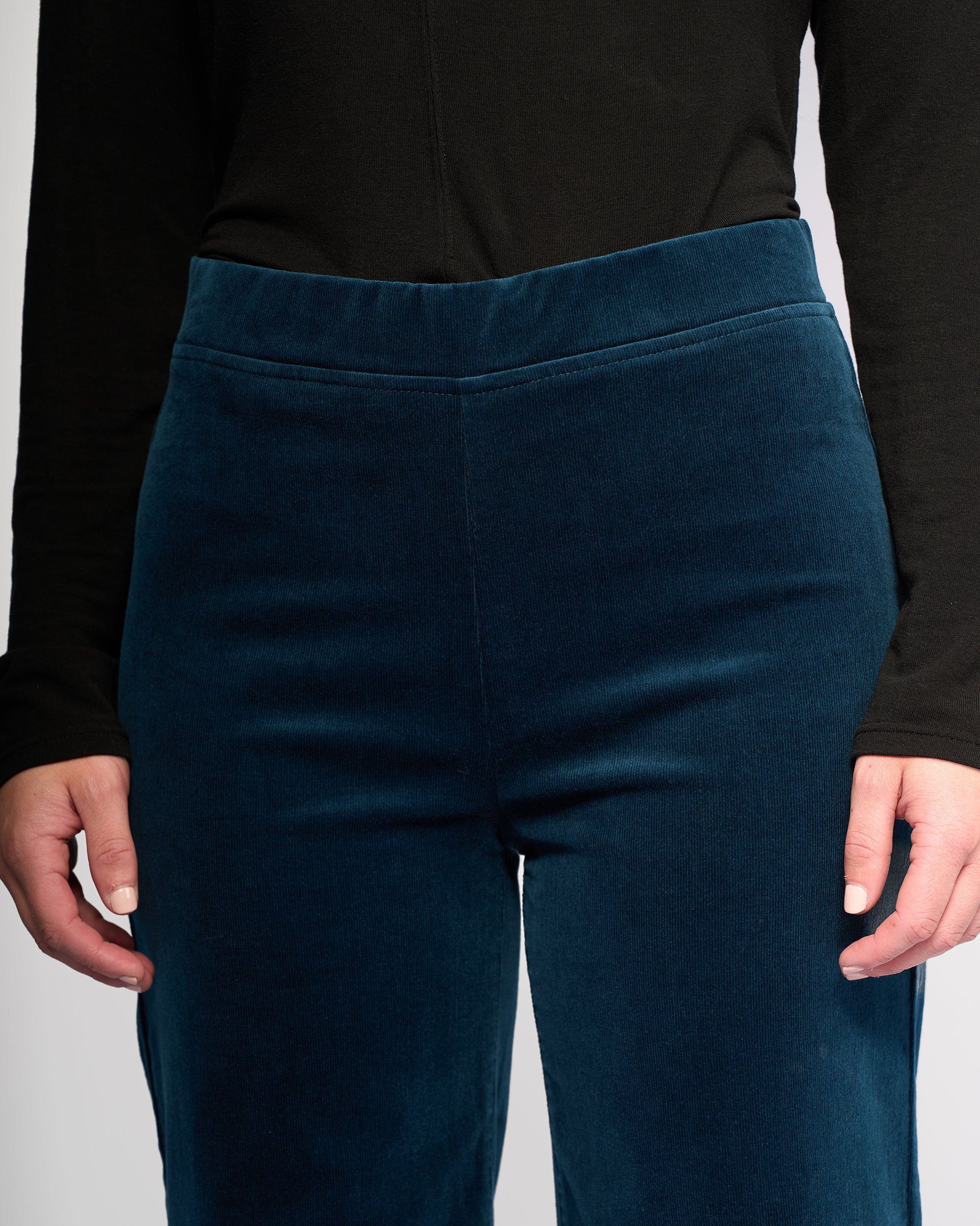 A person wearing a long-sleeve black top and Vassalli’s Loft Cord Pull On pants in Petrol, wide-leg style with a pull-on waist, shown from shoulders to mid-thigh, arms relaxed at their sides.