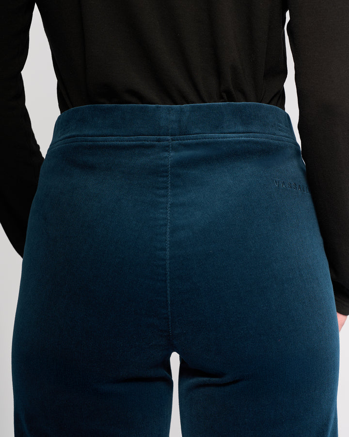 A person wearing a black long-sleeve top and Vassalli Loft Cord Pull On pants in Petrol, shown from the back at waist height, with subtle branding visible near the pull-on waist.