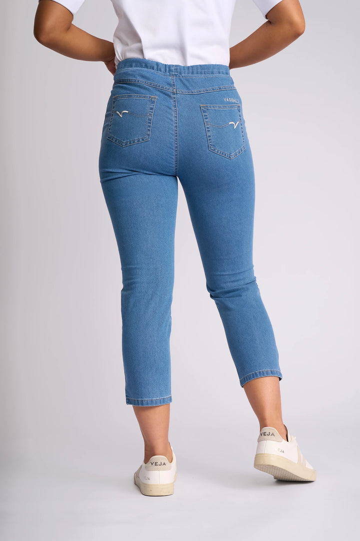 A person wearing the Vassalli Harbour 7/8 Pant in Light Denim (Contrast Stitch), paired with a white shirt and white VEJA sneakers, stands with their back to the camera against a plain background.