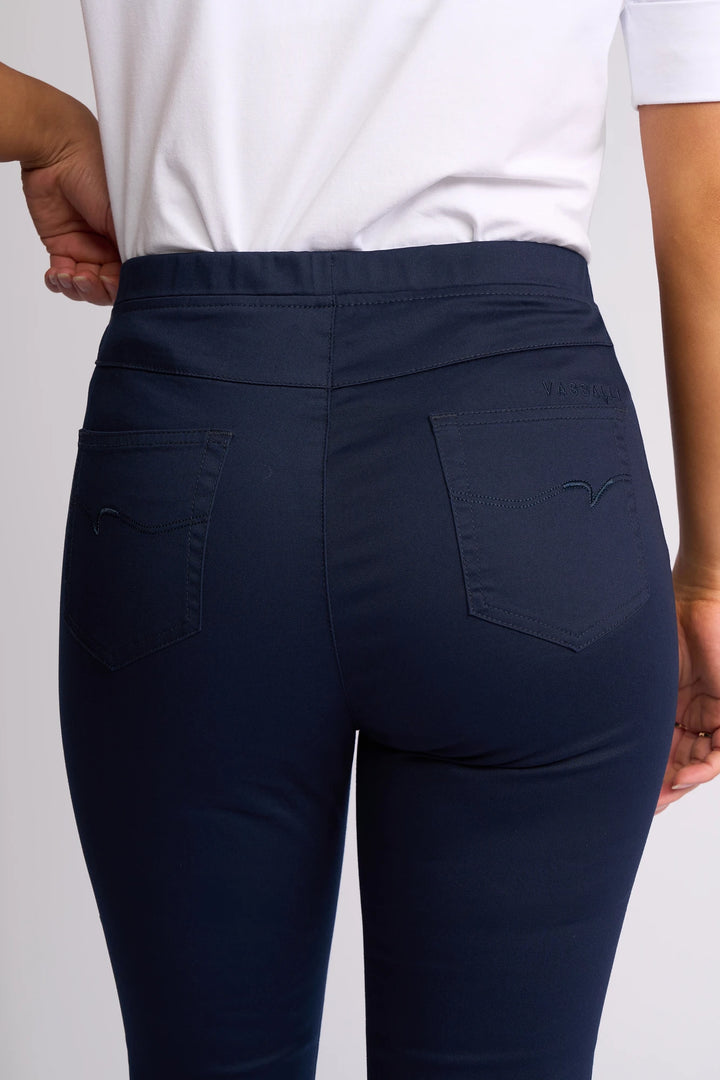 A person is shown from the back wearing a white shirt and Vassalli’s Harbour 7/8 Pant in Navy, with one hand resting on their hip. The fitted pants, crafted from stretch fabric, feature two back pockets and a skinny-leg pull-on design.