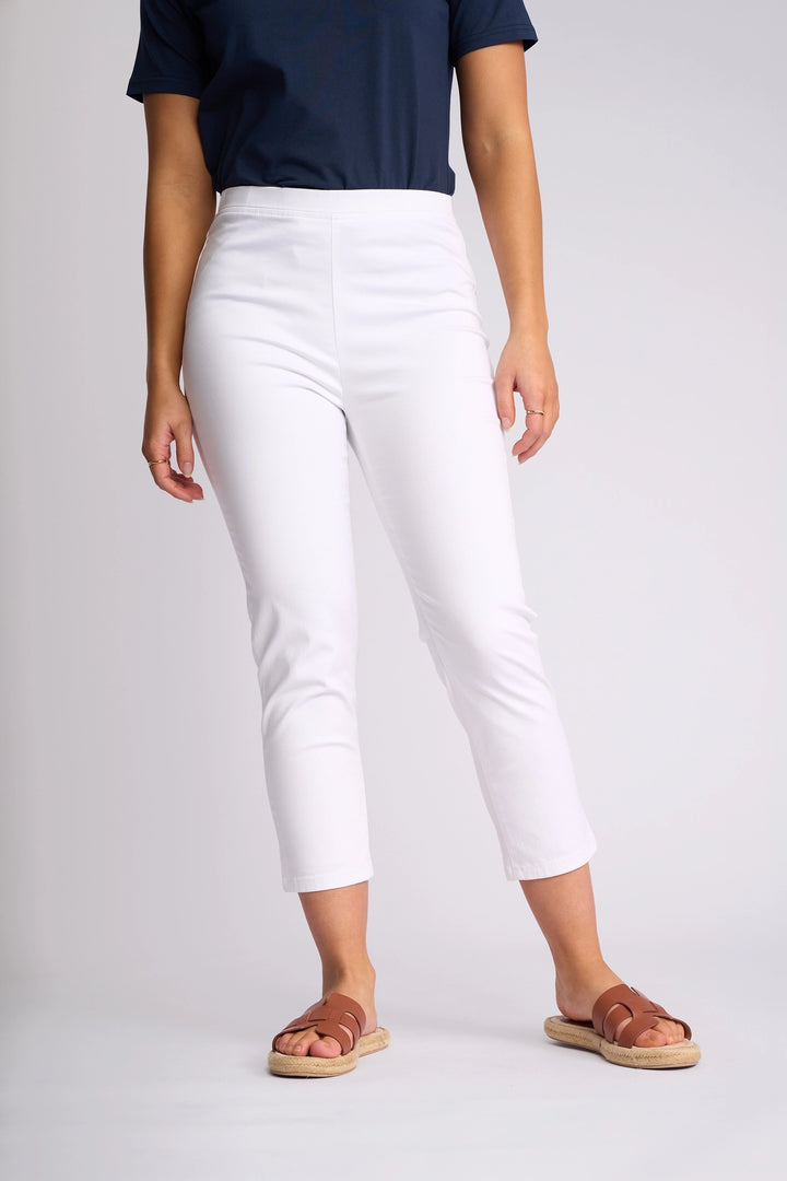 A person is wearing a navy t-shirt, the Vassalli Harbour 7/8 Pant in white—crafted from stretch fabric in a skinny-leg, pull-on style—and brown sandals, standing against a plain light background.