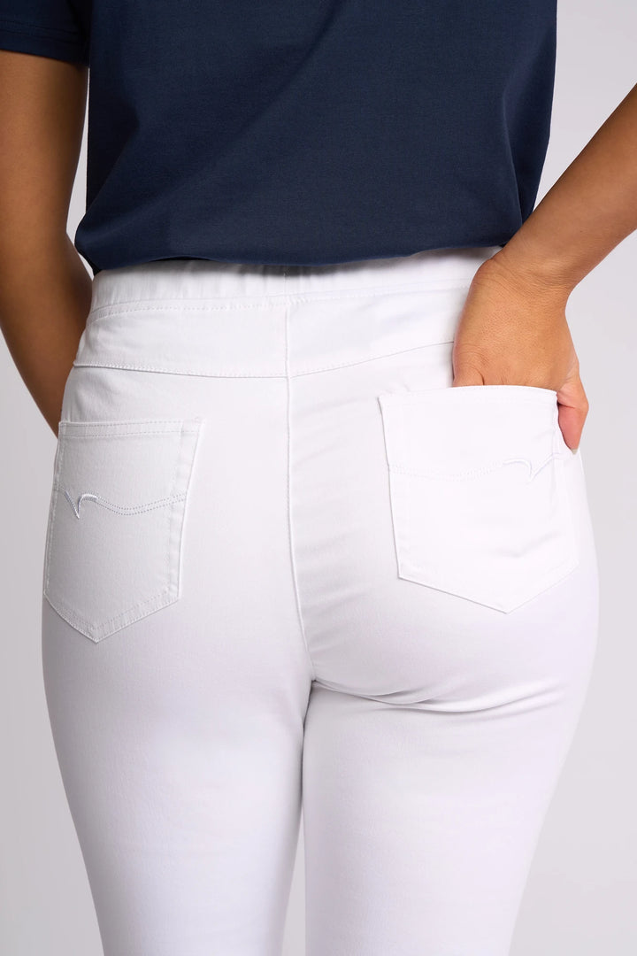 A person is shown from the waist down, wearing the Vassalli Harbour 7/8 Pant in White—a stretch fabric, skinny-leg pull-on style—with one hand placed in their back pocket.