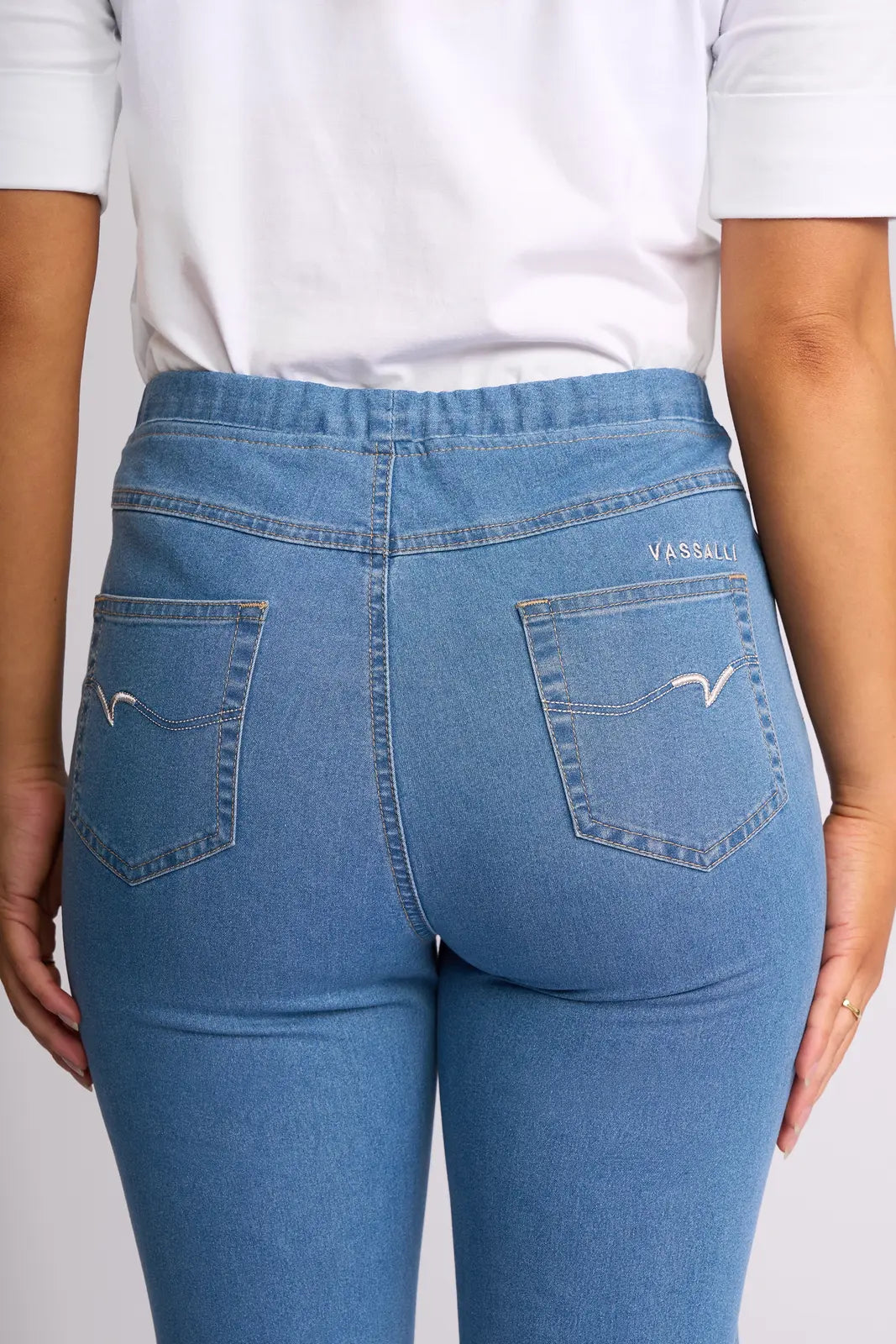 A person is shown from the back wearing Vassalli’s Sierra 7/8 Pant in Light Denim and a white shirt. These lightweight stretch denim jeans feature two back pockets with decorative stitching and the Vassalli brand name embroidered above the right pocket.